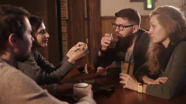 Две пары разговаривают в баре, сидя за столом с напитками — стоковое видео
