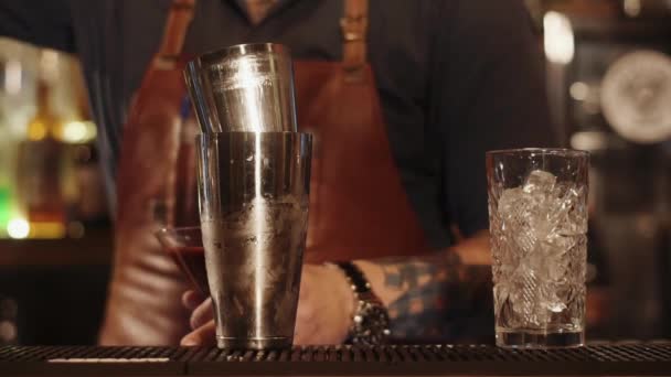 Barkeeper gießt Soße für einen Cocktail in einen Metallshaker, der auf einer Bar steht — Stockvideo