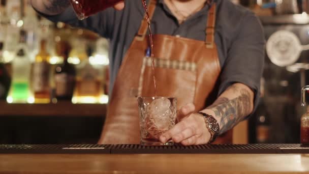 Barman está vertiendo bebida mezclada en un vaso con un gran trozo de hielo en un bar — Vídeos de Stock