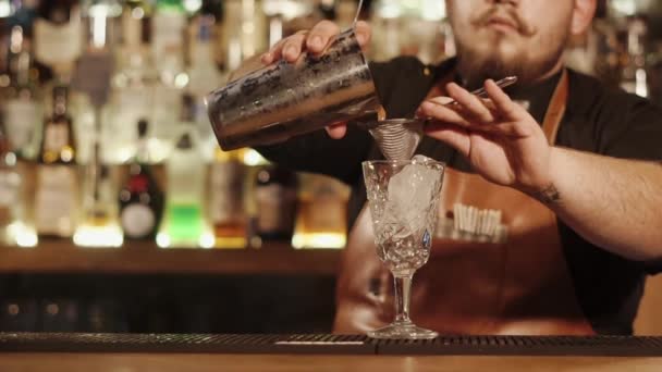 Cantinero está filtrando la bebida mezclada en un vaso para servir, primer plano de sus manos — Vídeo de stock