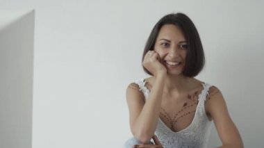 Neşeli Avrupa kadın vücudunda mehndi ile beyaz duvara yakın oturuyor