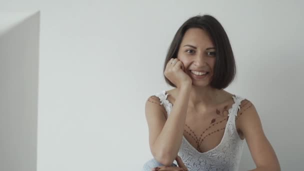 Fröhliche Europäerin mit mehndi am Körper sitzt neben weißer Wand — Stockvideo
