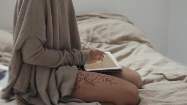 Студентка сидит на кровати и рисует на графическом планшете стилусом — стоковое видео