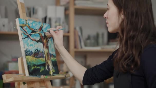 Femme dessine des détails sur l'image par des peintures en studio artistique — Video