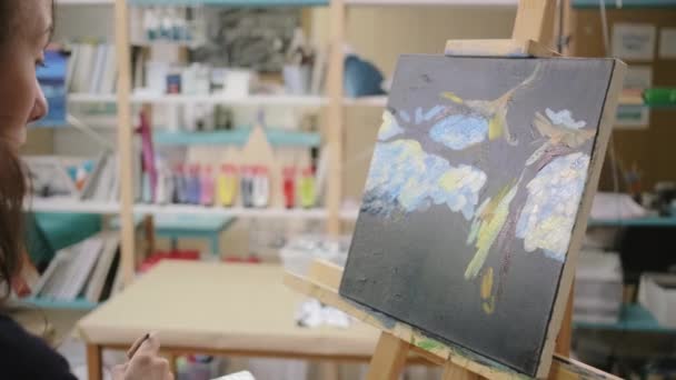 Νεαρή γυναίκα εργάζεται στο στούντιο τέχνης, ζωγραφίζοντας μια εικόνα, κοντινό πλάνο — Αρχείο Βίντεο
