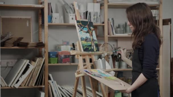 Художница работает в своей творческой студии, рисует картины — стоковое видео