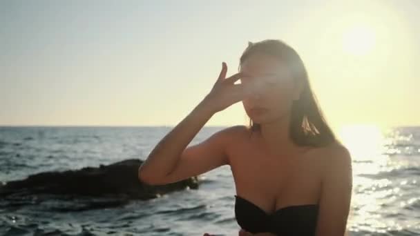 Mulher está massageando rosto com creme, sentado na praia do mar — Vídeo de Stock