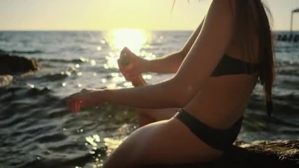 Mujer está rociando loción protector solar en la piel de la mano sentado en el mar de playa — Vídeos de Stock