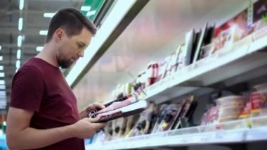 Alışveriş yapan adam iki paket sosisi süpermarkette karşılaştırıyor.