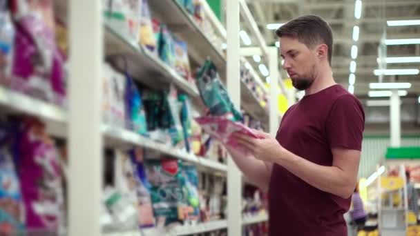 Hombre está leyendo inscripciones en paquete de alimentos para mascotas en el supermercado — Vídeos de Stock