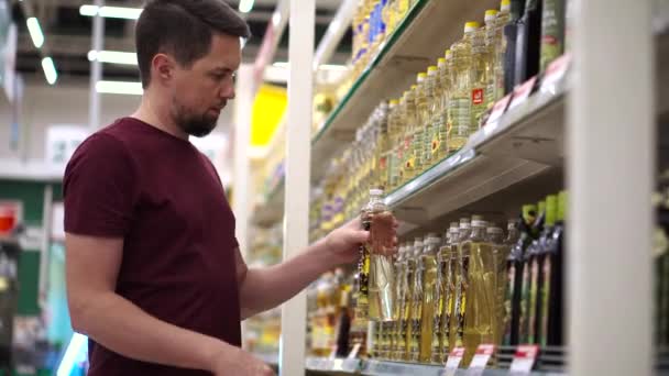 Muž nakupující bere láhve se slunečnicovým olejem v potravinové uličce v supermarketu — Stock video
