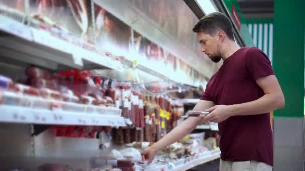 Comprador hombre está tomando paquetes de salchichas en el supermercado — Vídeos de Stock