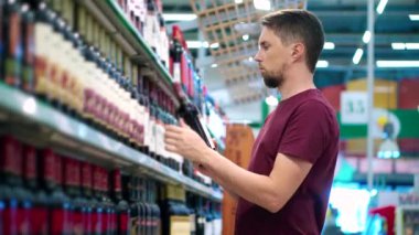 Adam süpermarketteki kırmızı şarabı seçiyor.