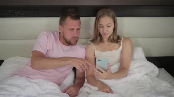 Junges Paar surft auf Handy im Bett liegend im Internet — Stockvideo