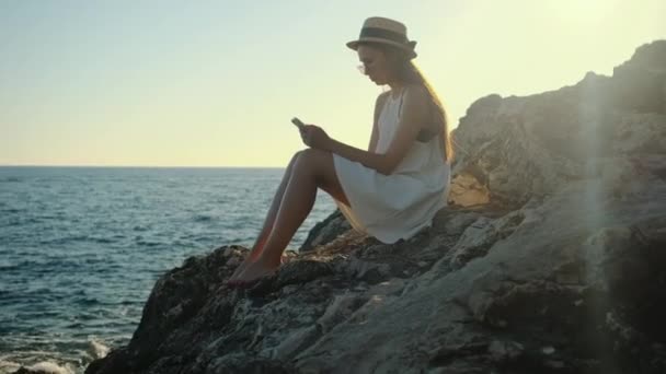 Chica disfrutando del tiempo a solas. Ella sentada en las rocas con móvil — Vídeos de Stock