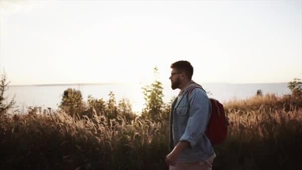 Muž kráčí po přírodě v blízkosti pole a moře ve slunečný den — Stock video