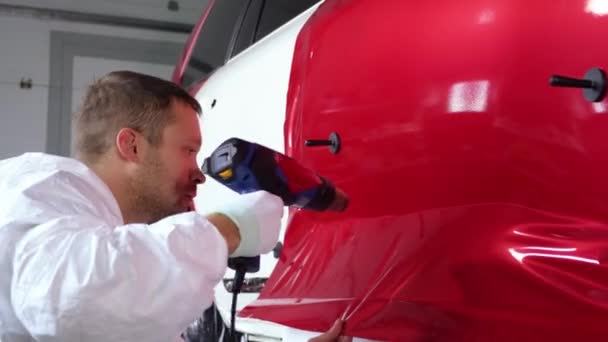 L'uomo operaio sta riscaldando il nastro in vinile dal ventilatore e fissando sulla porta dell'automobile — Video Stock