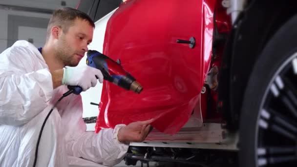 Férfi melegít vinil szalag ventilátor és rögzíti az autó karosszéria — Stock videók