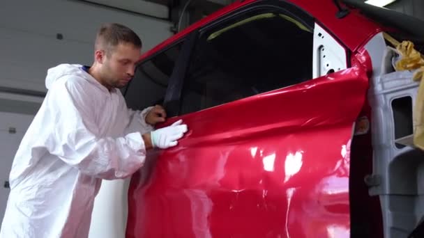 Arbeider man streelt kleurstof op auto lichaam met de hand in handschoen in auto service — Stockvideo