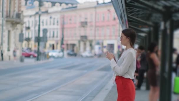 Kvinna använder smartphone stående på spårvagnstationen i staden — Stockvideo