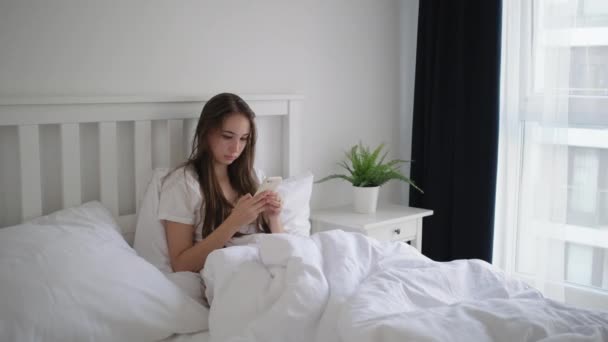 Kobieta używa smartfona leżącego w łóżku w godzinach porannych — Wideo stockowe