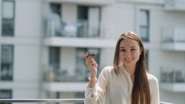 Frau winkt Autoschlüssel in der Hand und lächelt auf Balkon — Stockvideo