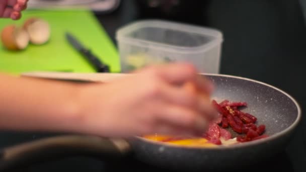Человек готовит яичницу с колбасой на сковороде, разбивая скорлупу — стоковое видео
