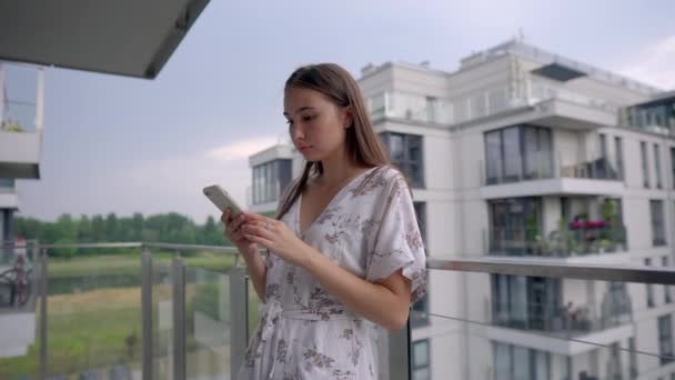 Mujer está viendo vídeo en la pantalla del teléfono móvil de pie en el balcón — Vídeo de stock