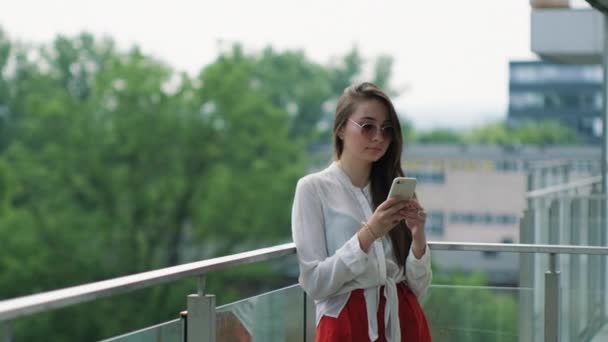 Vrouw staat op het balkon en het gebruik van smartphone in de zomer — Stockvideo