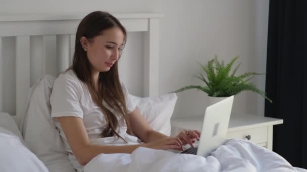 Frau ruht sich morgens im Bett aus und tippt Nachrichten auf Laptop — Stockvideo