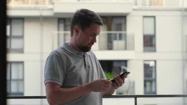 Чоловік використовує смартфон, стоїть на терасі будинку, натискаючи — стокове відео