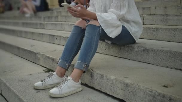 Девушка с мобильным телефоном сидит на лестнице — стоковое видео