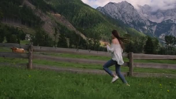 Ragazza di campagna è in esecuzione in fattoria nei prati alpini con mucche pascolo — Video Stock