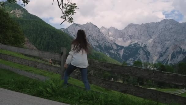 Female traveler is walking near fence of meadows in Alps, looking on mountains — Stock Video
