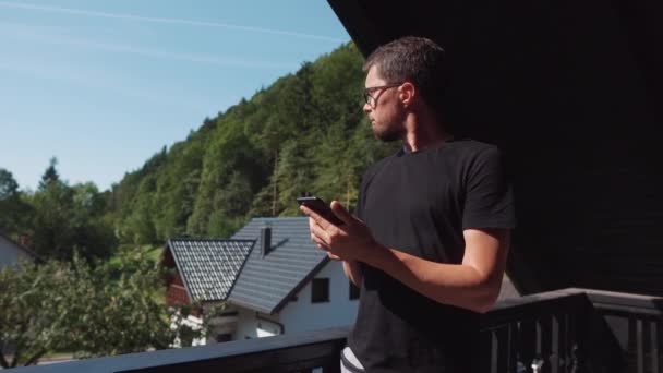 Uomo sta inviando un messaggio dal telefono cellulare in piedi sul balcone del cottage — Video Stock