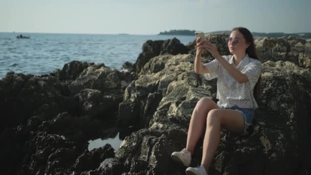 Chica disfrutando de la vista al mar y tomar fotos móviles de olas rompiendo — Vídeos de Stock