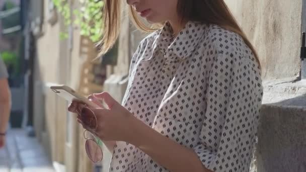 Female city dweller is typing message in cell phone on street — Stock Video