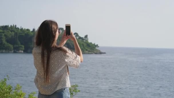 Vrouwelijke reiziger fotografeert uitzicht op zee per smartphone — Stockvideo