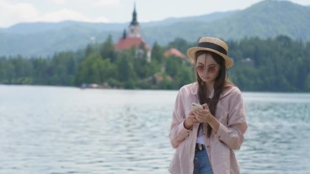 Ung kvinna med smartphone vid sjön Bled i Slovenien — Stockvideo