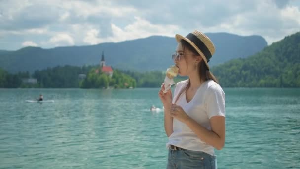 Jonge vrouw eet ijs aan de oever van het meer van Bled in Slovenië — Stockvideo