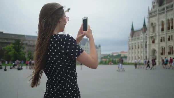 Женщина-туристка фотографируется на смартфоне венгерского парламента — стоковое видео