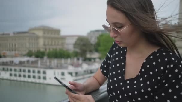 Дівчина зі смартфоном на мосту у вітряний день — стокове відео