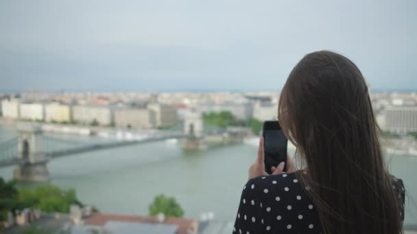 Туристка фотографирует по мобильному телефону панораму Будапешта — стоковое видео