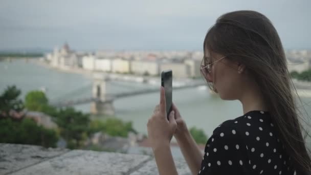 Девушка снимает городской пейзаж Будапешта с мобильного телефона — стоковое видео