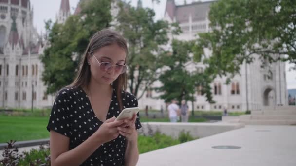 Mujer joven está enviando un mensaje por teléfono celular al aire libre — Vídeos de Stock