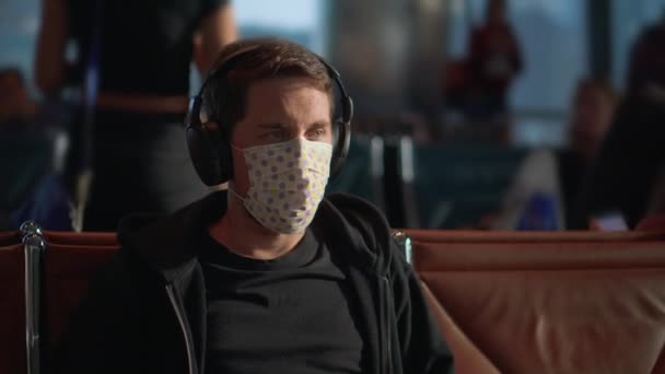 空港のコロナウイルスから安全になるためにマスクをしたヘッドフォンの男 — ストック動画