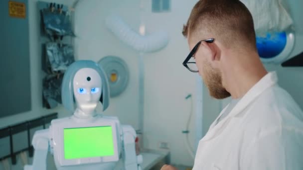 Robô está falando com engenheiro em laboratório, o homem está digitando em tablet — Vídeo de Stock