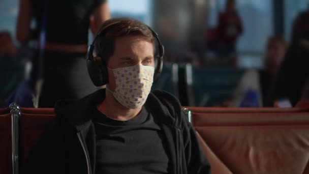 Человек в наушниках в маске, чтобы обезопасить себя от коронавируса в аэропорту — стоковое видео