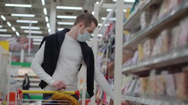 Erkek alışverişçi marketten yiyecek alıyor, koruyucu maskesi var.