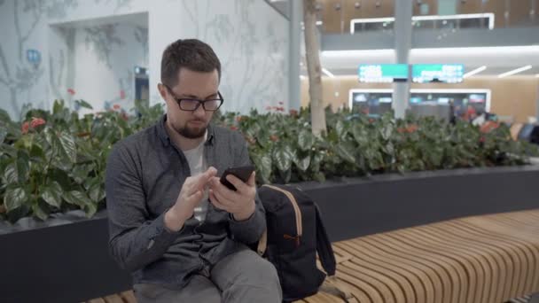 Путешественник с рюкзаком и мобильным в зале ожидания аэропорта — стоковое видео